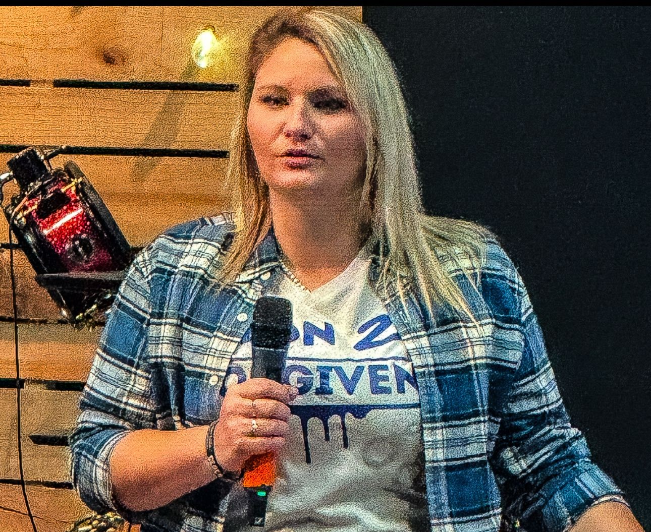 Person speaking into a microphone, wearing a flannel shirt and graphic tee.