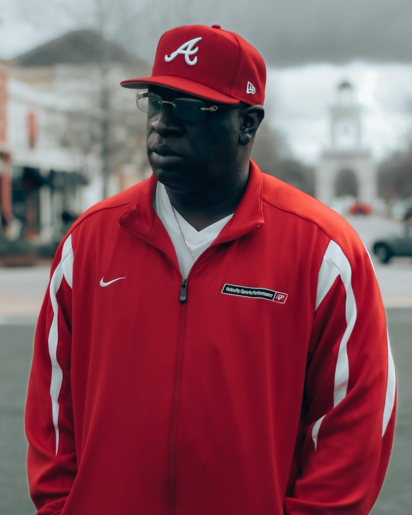 Person wearing a red jacket and matching red cap standing outdoors with blurred buildings in the background.